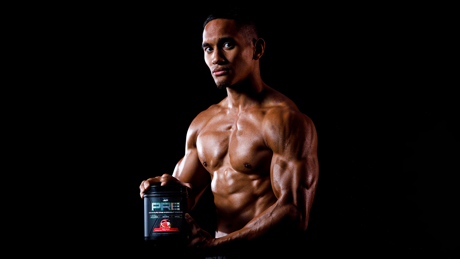 Lean bodybuilder with defined chest and arms presents JYM PRE Tiger's Blood pre-workout tub, illustrating pump-enhancing supplement article.