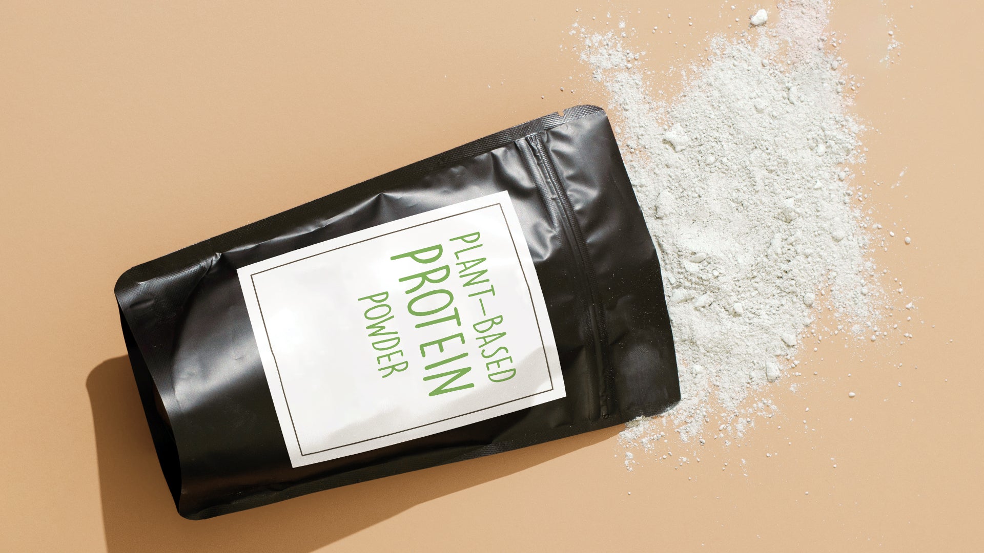 Overhead view of tilted black zip pouch with green Plant-Based Protein Powder label and powder spilling out onto tan background.