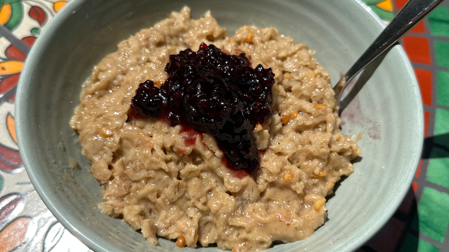 Peanut Butter ‘N Jelly Pro JYM Oats served in a gray bowl with berry jam on top and a spoon resting inside.
