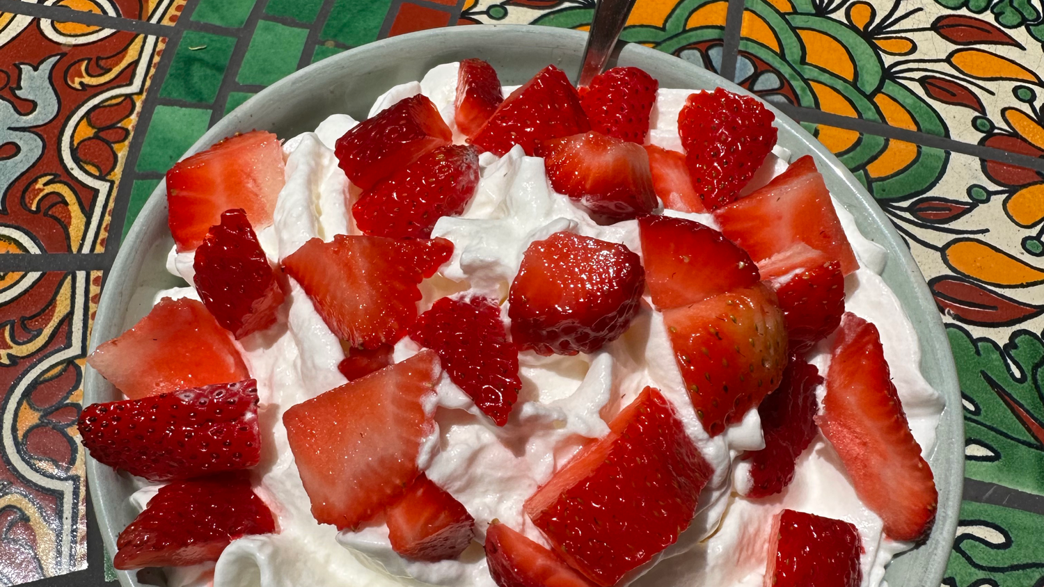Close-up of strawberry pieces over whipped cream in a white bowl with spoon, for Strawberry Shortcake Pro JYM Oats.