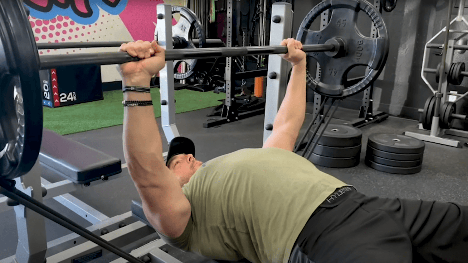 Lifter in olive tee gripping barbell with 45-pound plates at chest level on flat bench, A Bigger Bench Press with Bands.