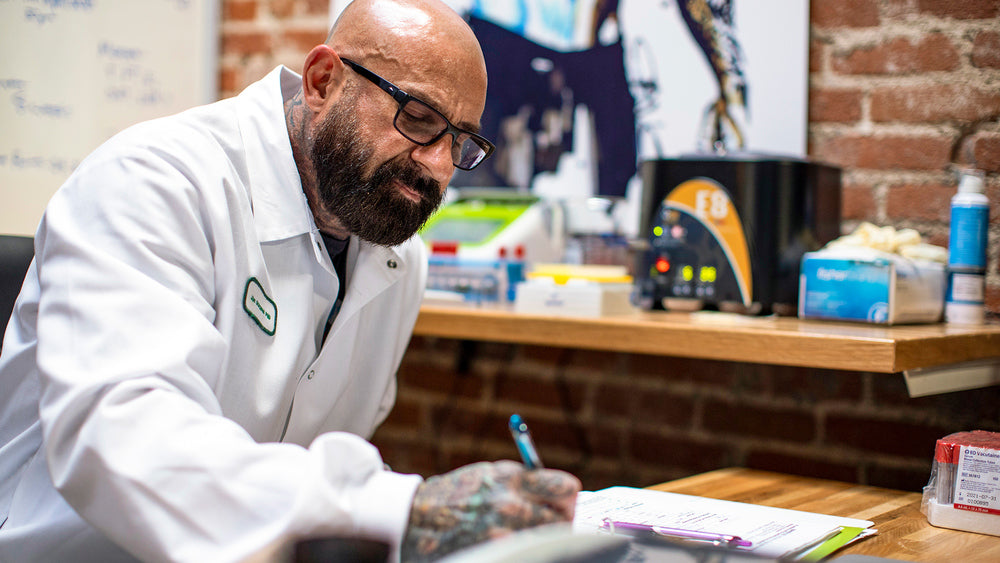 Bald bearded doctor in glasses and lab coat writing in notebook at wooden desk with medical devices, Beta-Alanine Benefits.