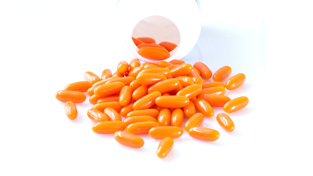 Mound of orange oval CoQ10 softgels tumbling from a clear jar onto a white surface, for article on CoQ10 basics.