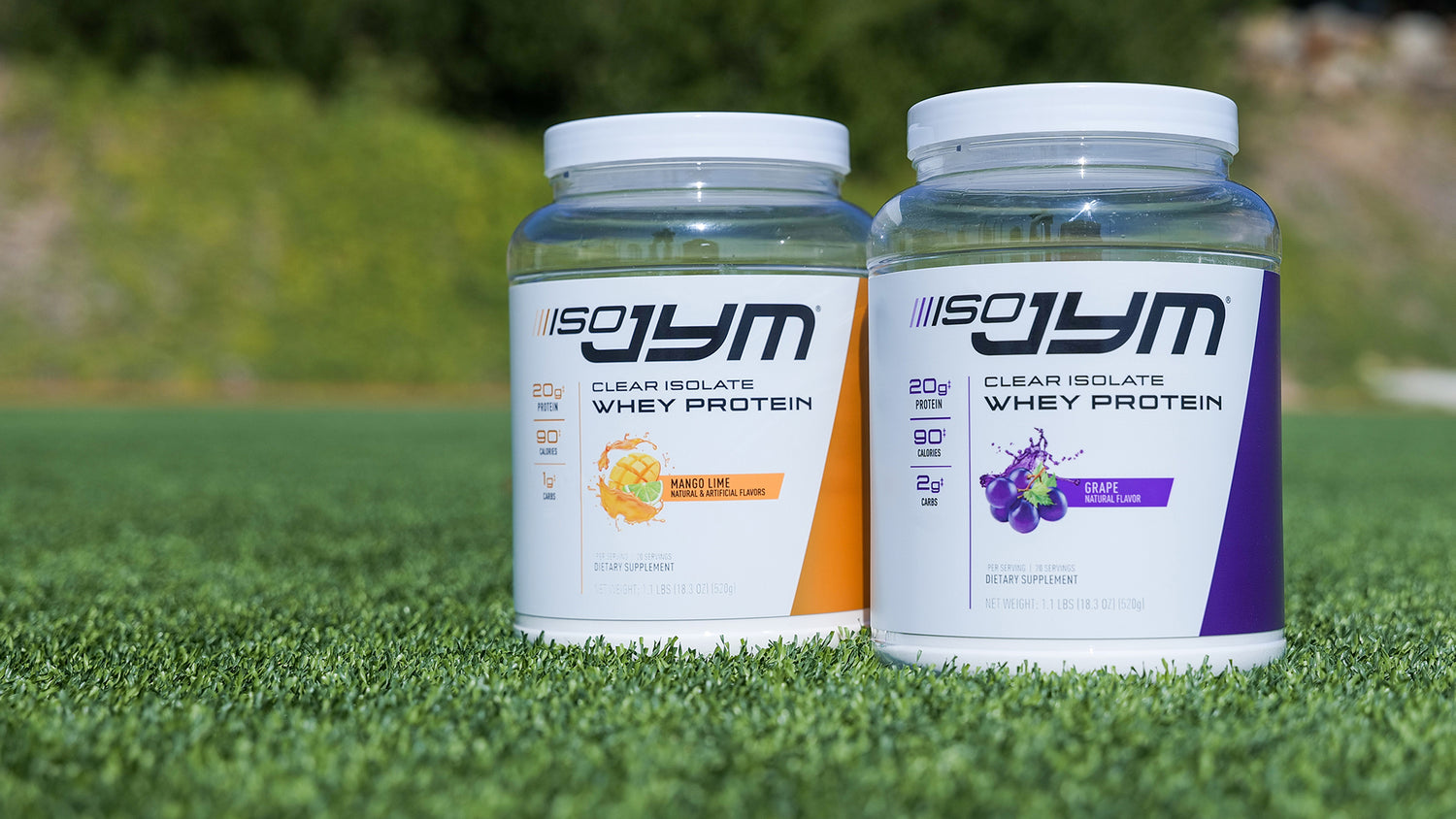 Mango Lime and Grape Iso JYM Clear Whey Protein Isolate containers on artificial turf with blurred shrubs in background.