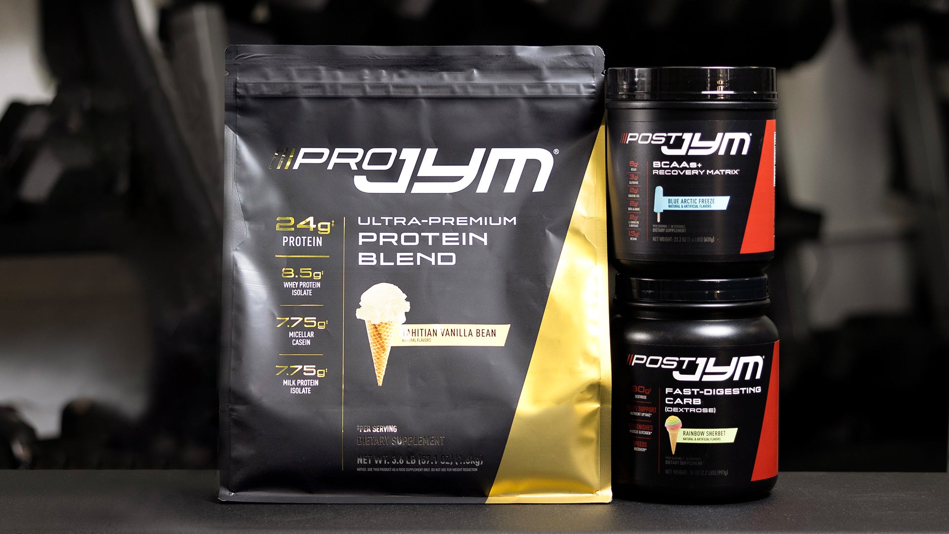 Pro JYM vanilla protein bag displayed with Post JYM Blue Arctic Freeze BCAA tub stacked on Rainbow Sherbet carb tub.