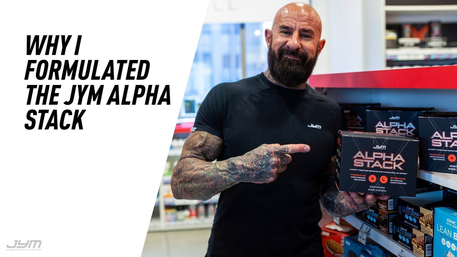 Jim Stoppani in a black JYM shirt pointing at an Alpha Stack box on a store shelf, from Why I Formulated the JYM Alpha Stack.