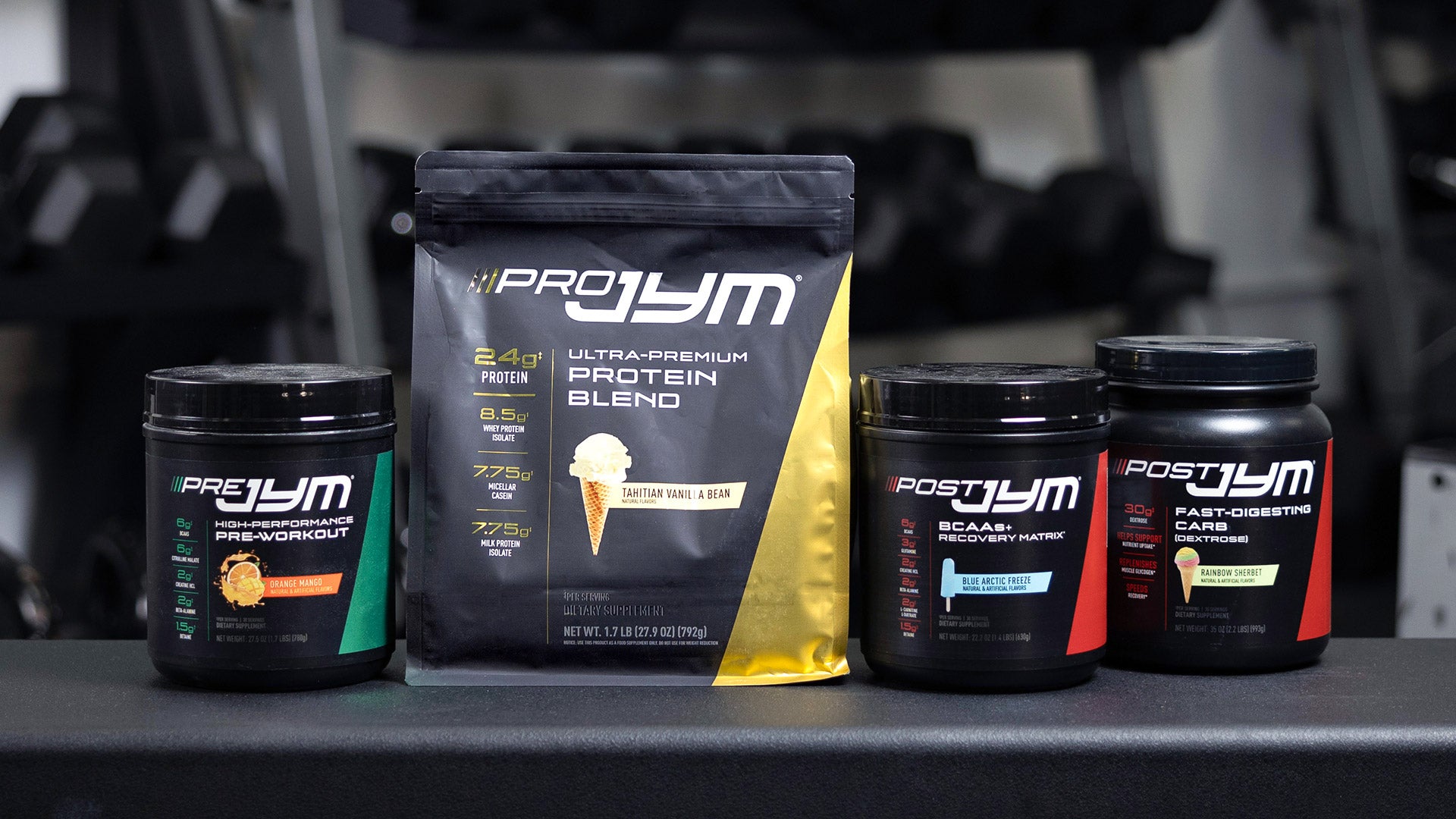 JYM System Stack lineup on gym counter: Pre JYM, Pro JYM protein pouch, Post JYM BCAAs, and Post JYM Fast-Digesting Carb.