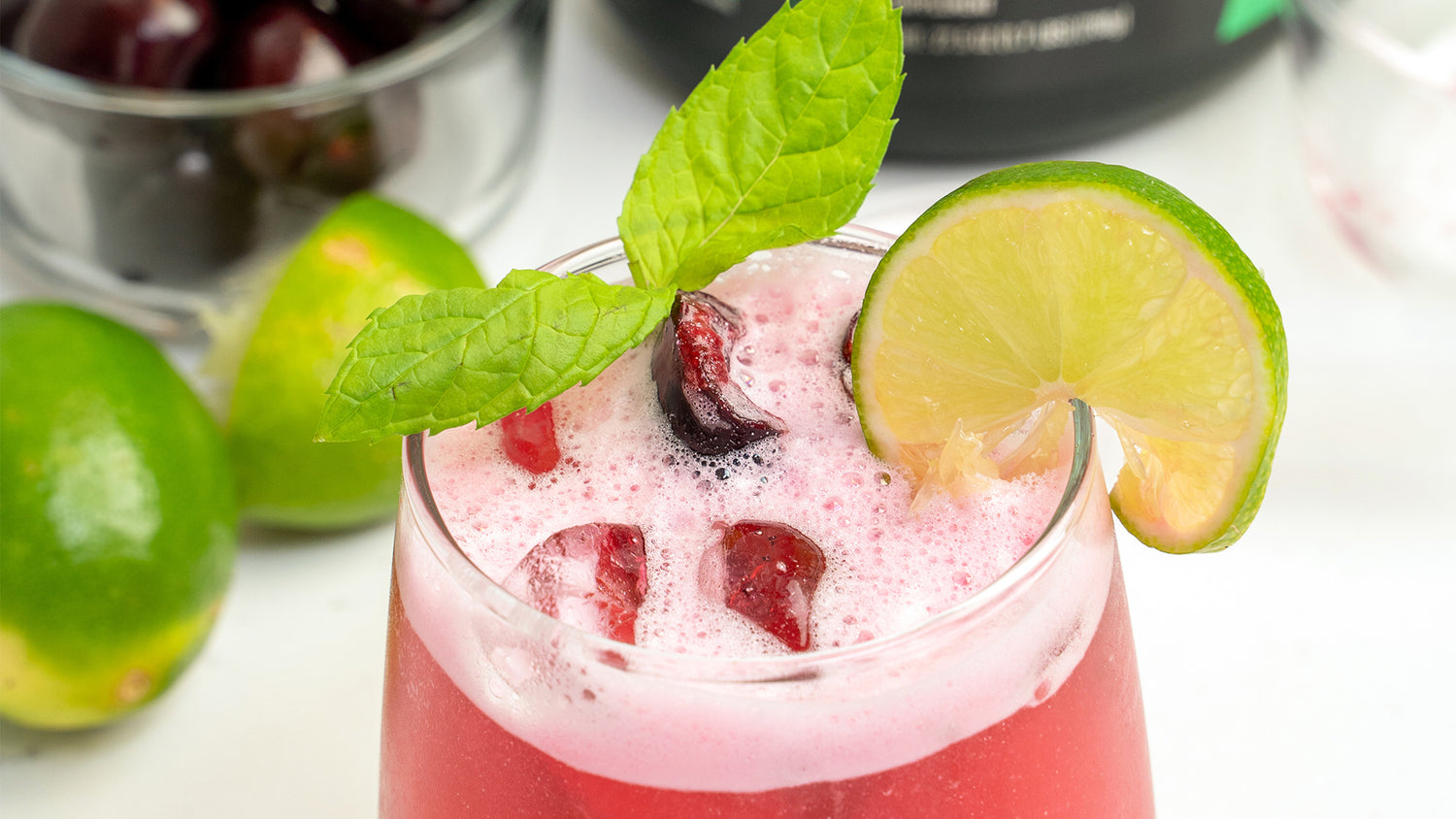 Cherry Lime Pre JYM Mocktail in a glass with pink foam, cherries, mint leaves, and a lime wheel garnish.