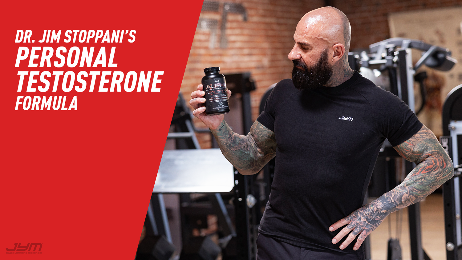 Tattooed man in black JYM shirt holding Alpha JYM capsule bottle in gym—Dr. Jim Stoppani's Personal Testosterone Formula.