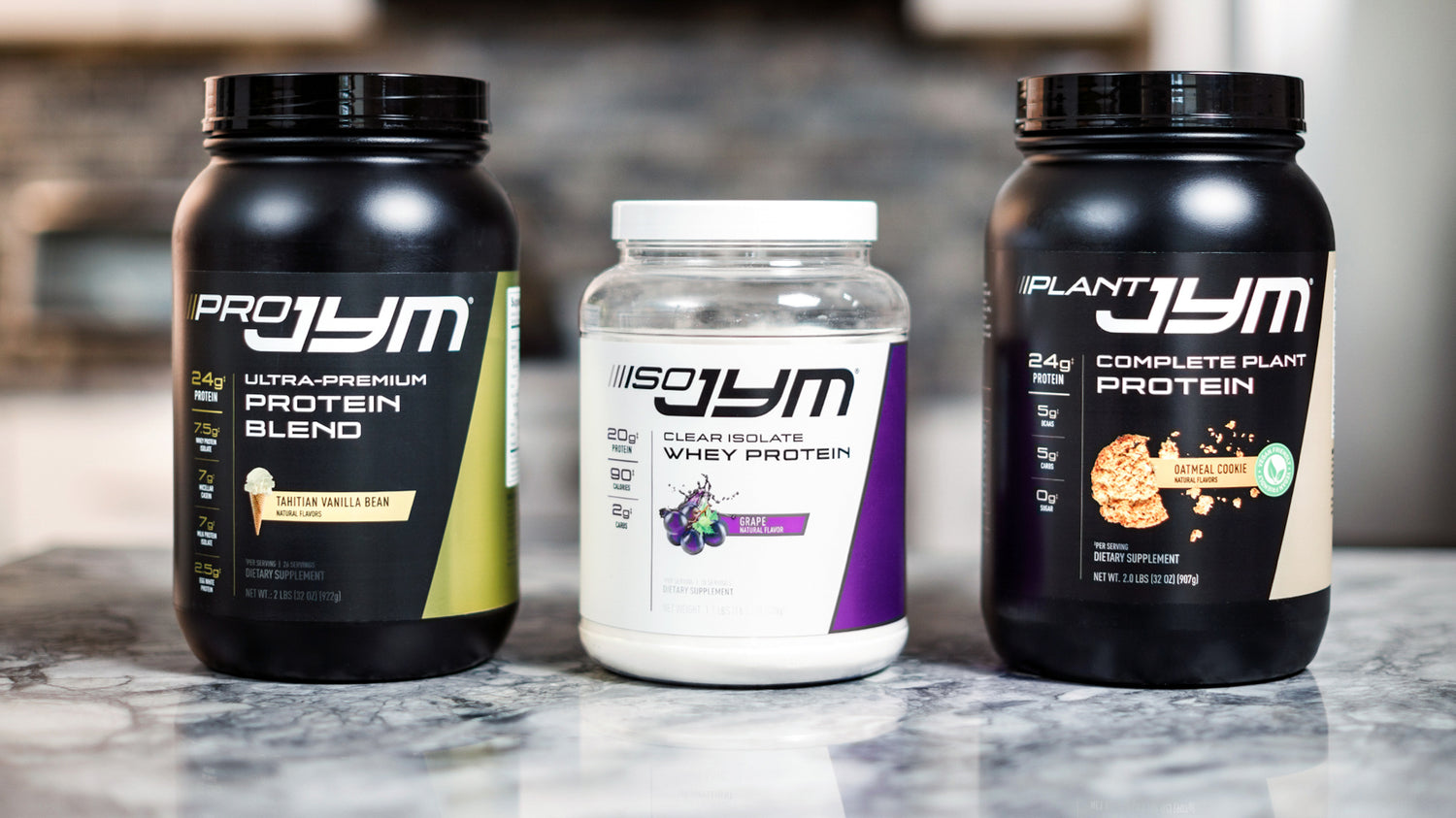 Pro JYM, Iso JYM Grape, and Plant JYM Oatmeal Cookie protein tubs lined up on marble counter for Protein Powder Users Guide.