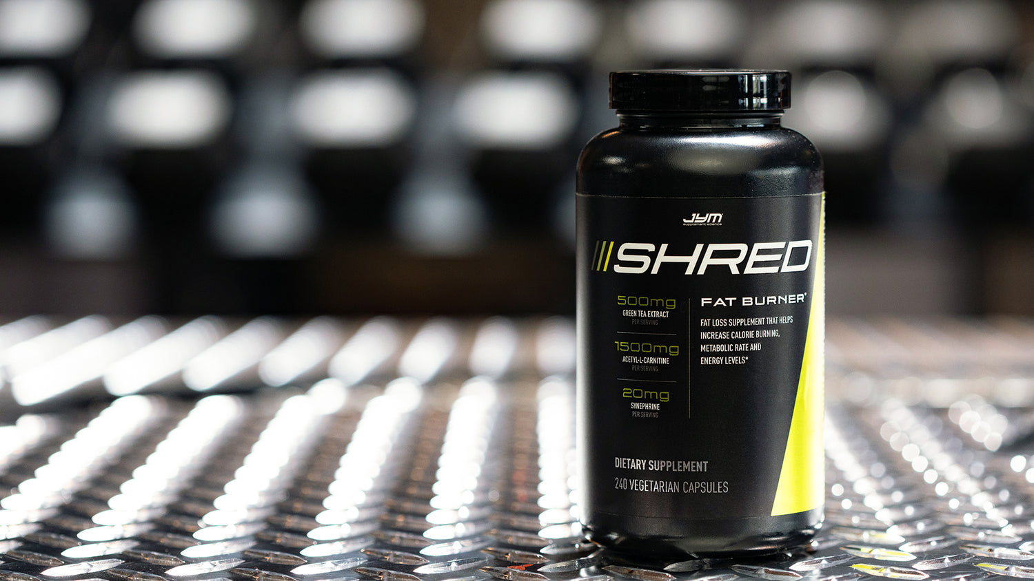Black Shred JYM fat burner bottle with green accents on diamond-plate gym floor, showing 240 vegetarian capsules label.