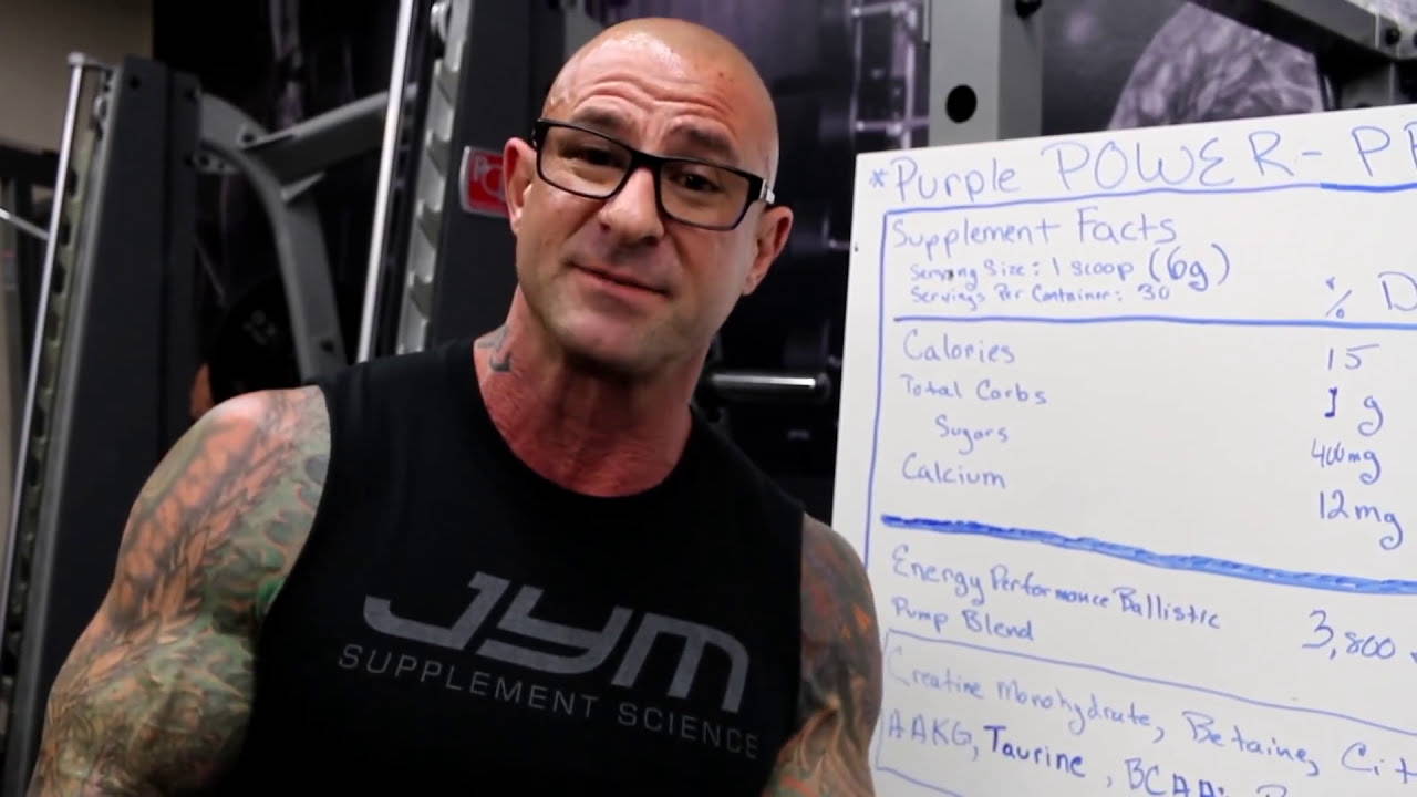 Tattooed man in JYM tank top next to whiteboard showing Pre JYM serving size, calories, and Pump Blend ingredients.