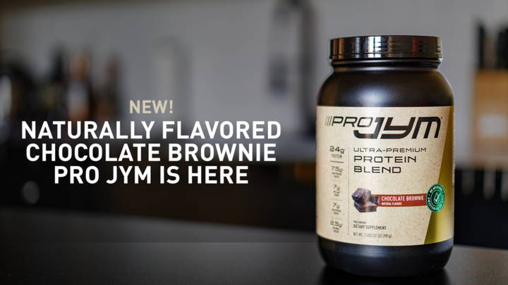 Pro JYM Chocolate Brownie protein blend tub on a kitchen counter announcing the new naturally flavored version.