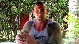 Close-up of Jim Stoppani in white JYM tank, arms crossed near face, outdoors, illustrating How Big Is Your PRE WORKOUT SCOOP article.