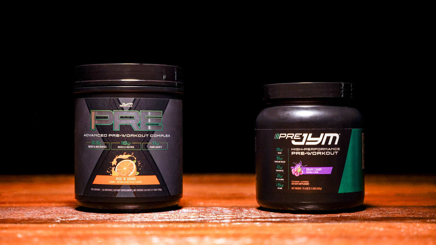 Pre JYM X Rise 'N' Grind orange tub beside Pre JYM Grape Candy tub on a wooden surface, labels facing forward.