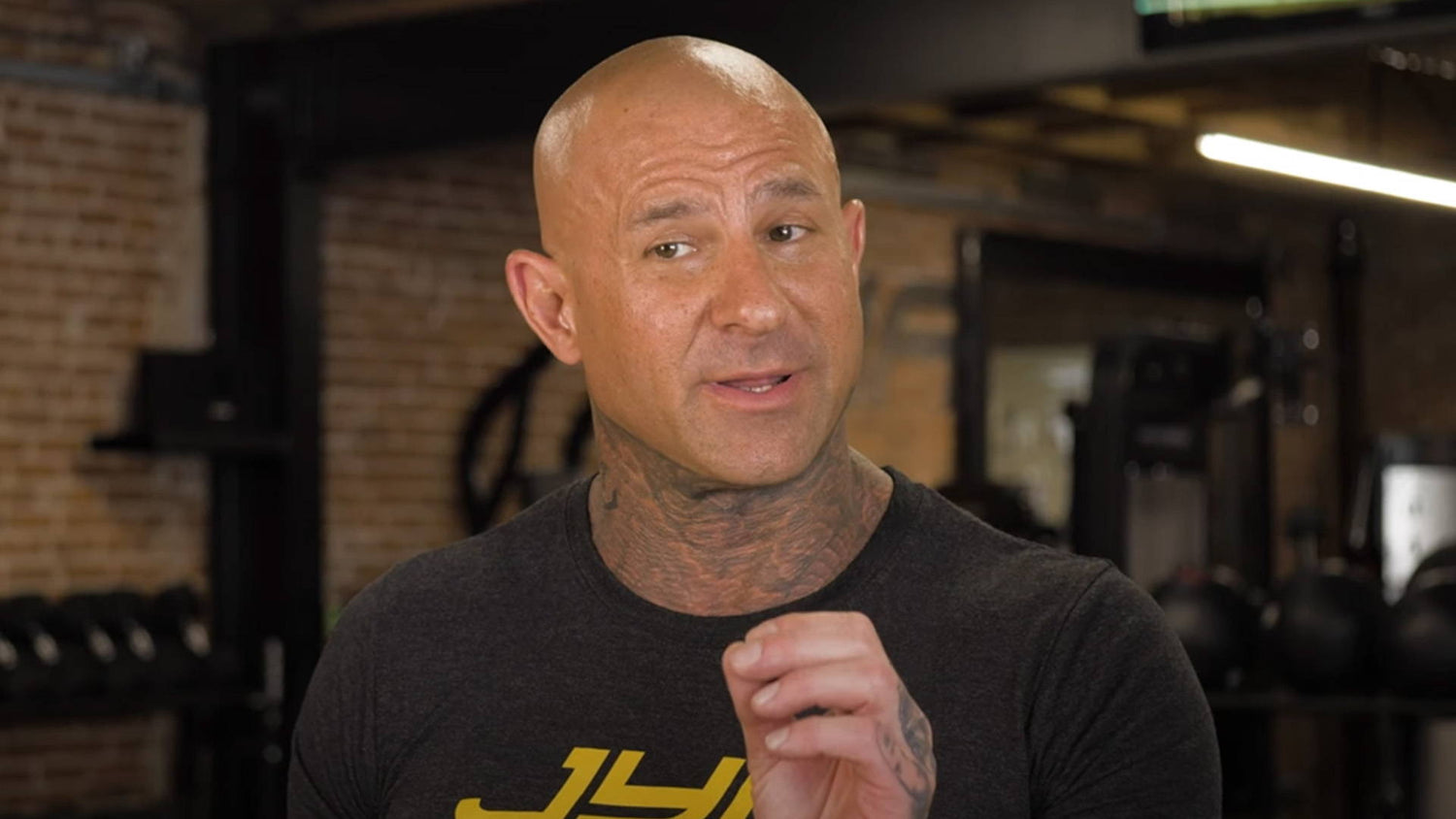 Jim Stoppani in black JYM t-shirt speaking in a gym with dumbbells and kettlebells, discussing key pre-workout ingredients.
