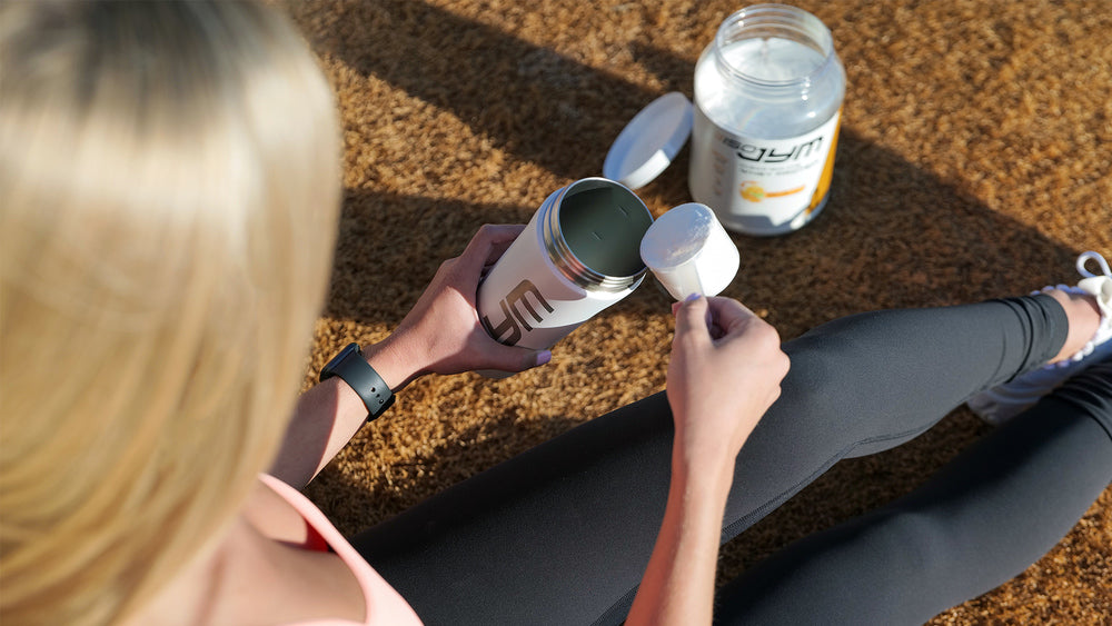 Woman seated on track pours scoop of ISO JYM powder into white JYM shaker, open tub beside her—Women's Nutrition and Supplement Guide.